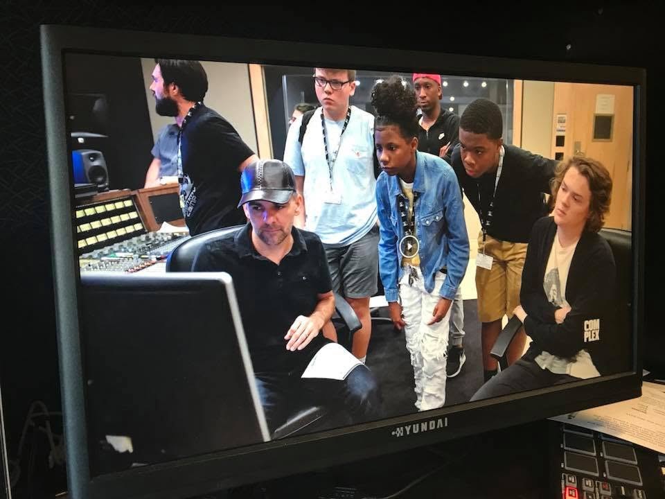 Nathan Adam seated at a console with GRAMMY Camp students standing behind him watching the screen