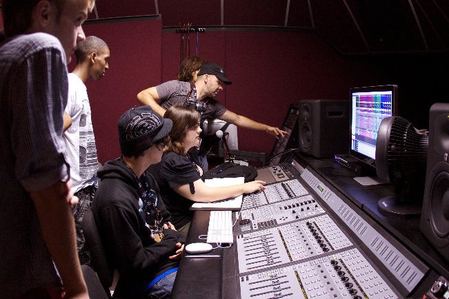 GRAMMY Camp students crowded around a recording console while Nathan Adam reaches across the desk