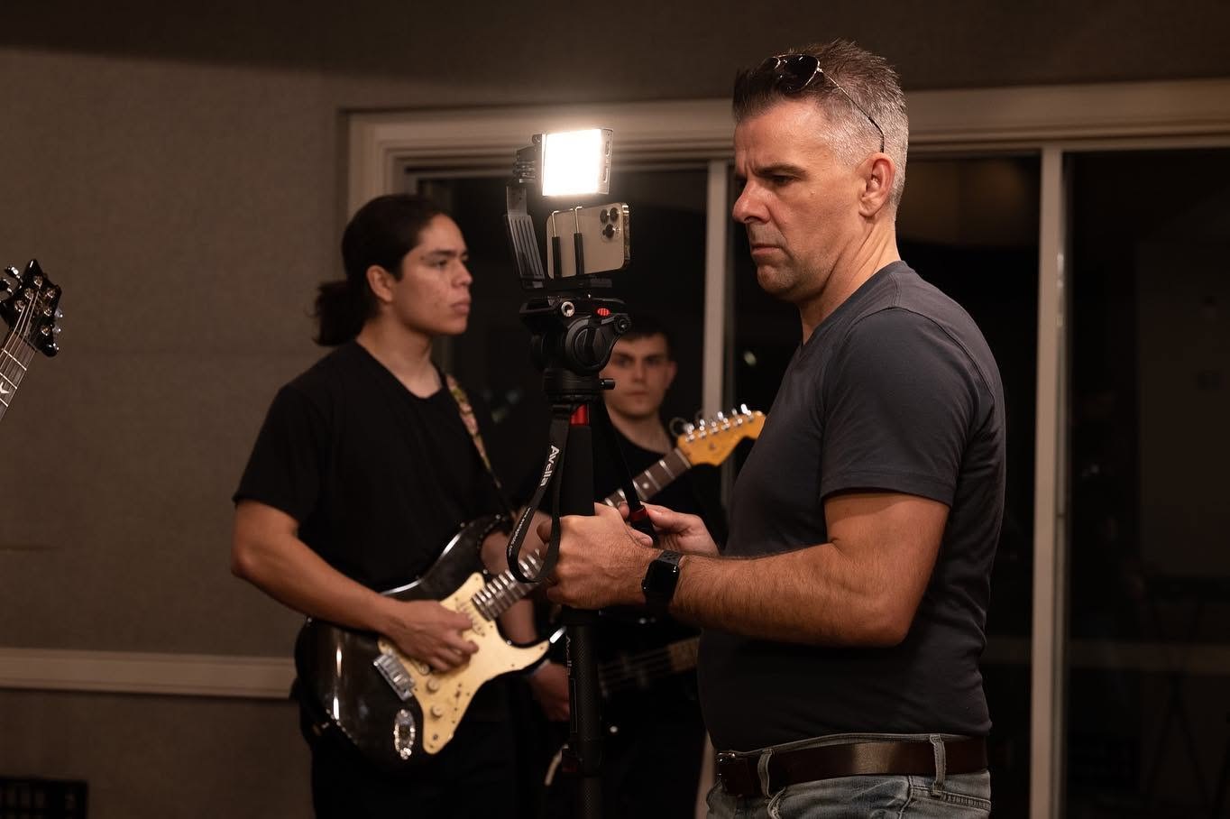 Nathan Adam adjusting a camera rig while a keyboard player performs in the background