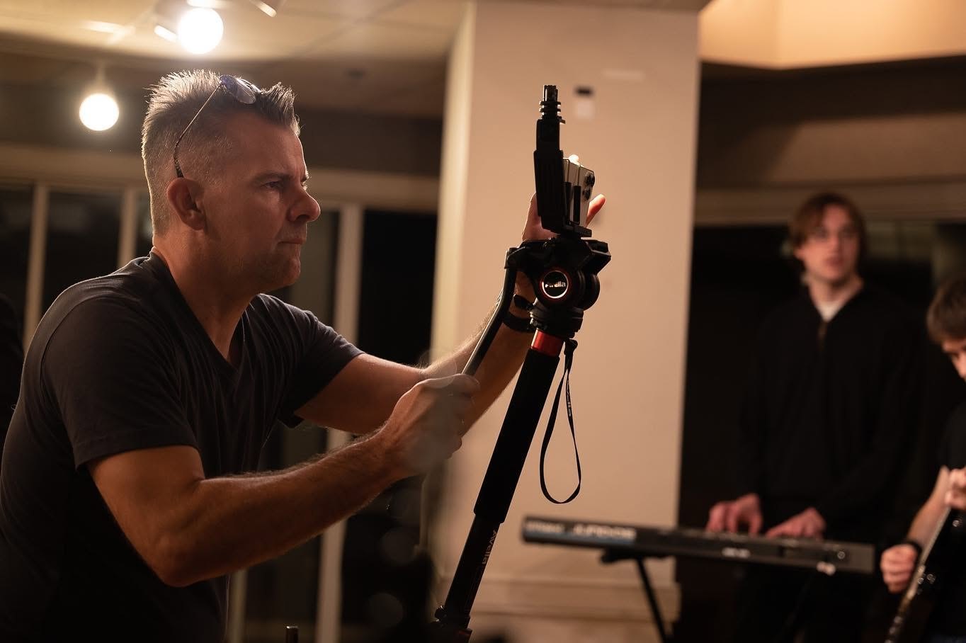 Nathan Adam operating a phone rig on a monopod while a guitarist plays behind him