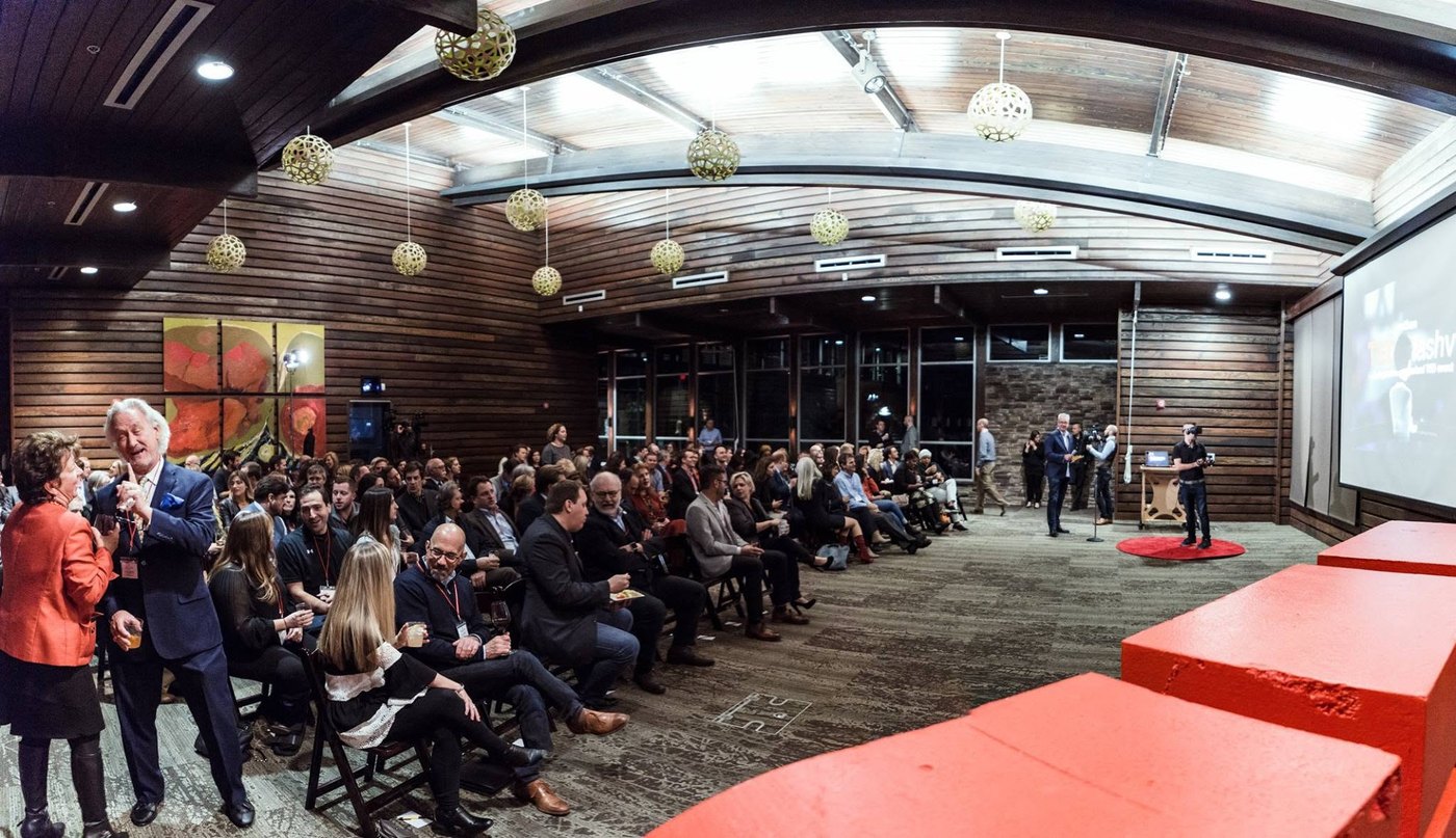 Wide view of the TEDxNashville room, a full audience seated facing the stage and the red TEDx blocks in the foreground