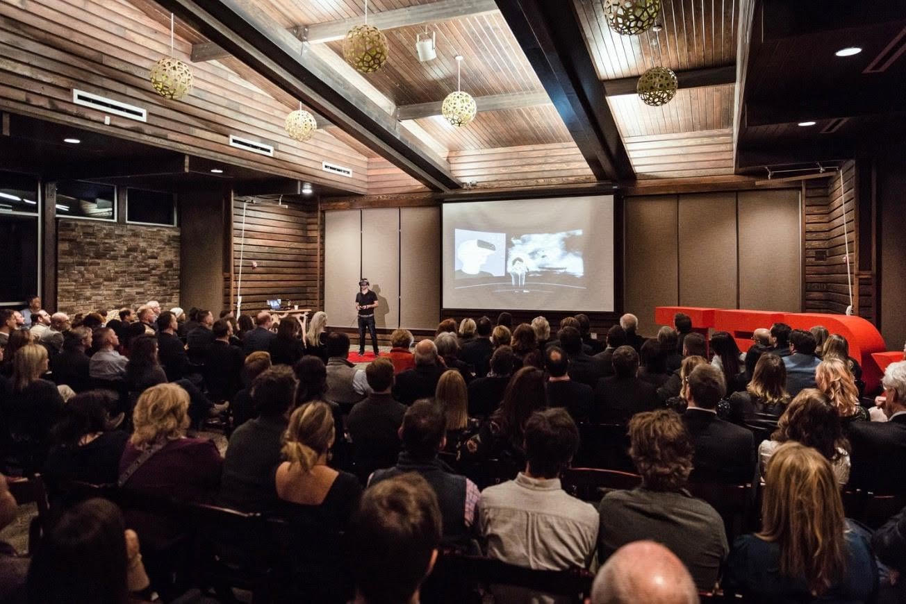 A TEDxNashville audience seated in a wood-panelled room watching a speaker on the red stage