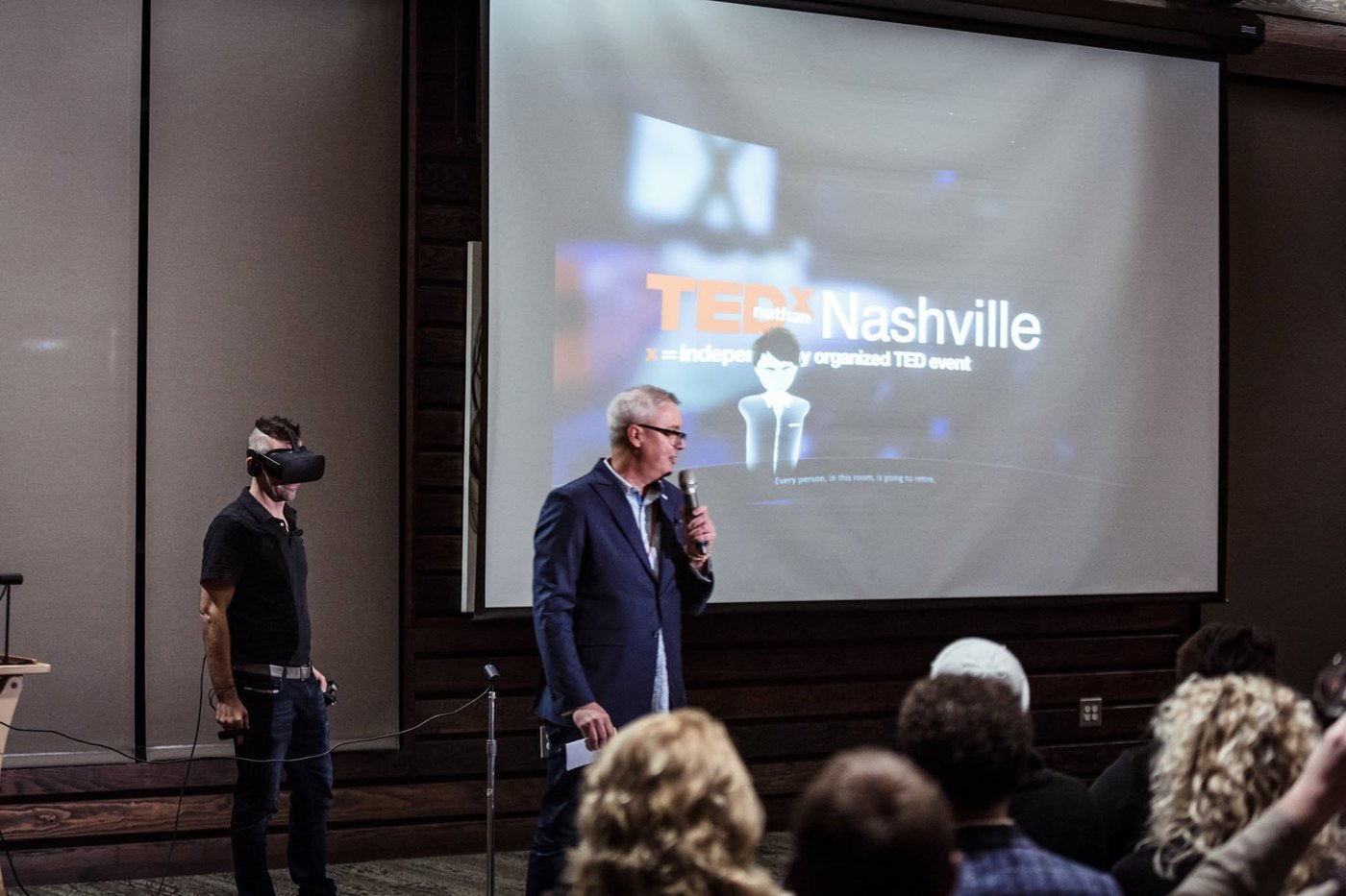 Nathan Adam standing in a VR headset while a host introduces him, the TEDxNashville title slide projected behind them